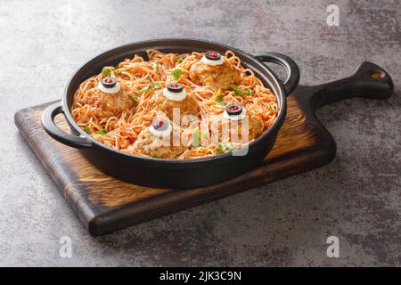 Gruseliges Halloween-Essen aus Fleischbällchen mit Monsteraugen und Pasta mit Tomatensauce in einer Pfanne auf dem Tisch aus der Nähe. Horizontal Stockfoto