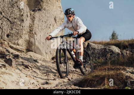 Ausgerüsteter Profi-Radler fährt mit seinem Mountainbike eine Piste hinunter, der Sportler fährt mit dem Fahrrad vom Berg herunter Stockfoto