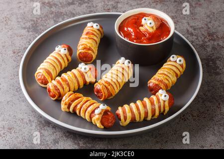 Lustige Wurstmumien im Teig mit Ketchup für die Halloween Party. Kindernahrung in Nahaufnahme auf dem Teller auf dem Tisch. Horizontal Stockfoto