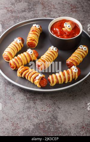 Gruselige Mumienwürste im Teig mit lustigen Augen auf dem Tisch aus der Nähe. Lustige Dekorationen. Halloween-Essen. Vertikal Stockfoto