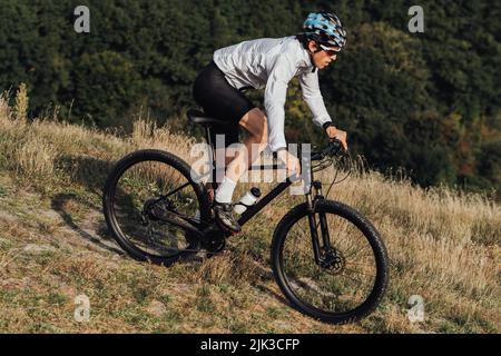 Ausgerüsteter Profi-Radler fährt mit seinem Mountainbike eine Piste hinunter, der Sportler fährt mit dem Fahrrad vom Berg herunter Stockfoto