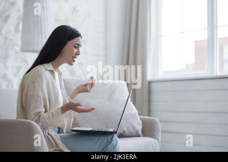 Junge schöne Frau allein zu Hause in Depressionen weinend, Brünette zu Hause sitzen und mit Laptop für Online-Beratungsgespräch mit Psychotherapeuten Stockfoto