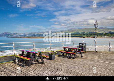 Picknicktische am Garth Pier in Bangor mit den Snowdonia Mountains und der Küste im Hintergrund, Gwynedd, Nordwales Stockfoto