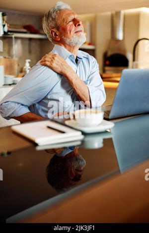 Ein älterer Mann sitzt in einem Café und hat Rückenschmerzen. Stockfoto