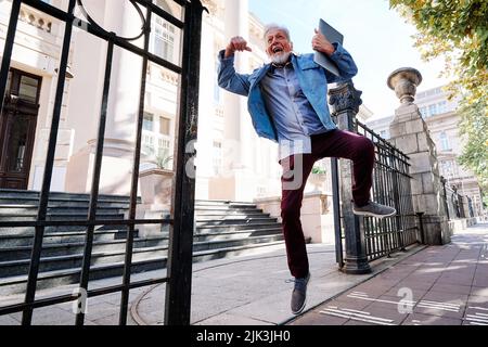 Ein glücklicher älterer Student im Umschulungsprogramm hat die Prüfung bestanden und er springt vor Freude und Glück. Stockfoto