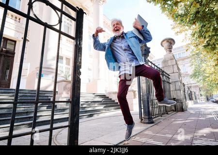 Ein glücklicher älterer Student im Umschulungsprogramm hat die Prüfung bestanden und er springt vor Freude und Glück. Stockfoto