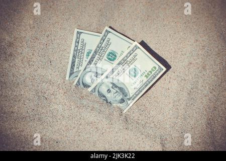 Gelddolare, die halb mit Sand bedeckt sind, liegen in der Nähe des Strandes. Dreihundert Dollar im Sand auf Meer oder Meer Strand begraben Konzept finanzieren Geld Urlaub entspannen Urlaub. Sonniger Sommer warmer Windtag. Stockfoto