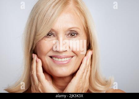 Nahaufnahme einer schönen älteren Dame, die ihre weiche, faltige Haut berührt. Beauty-Fotografie Stockfoto