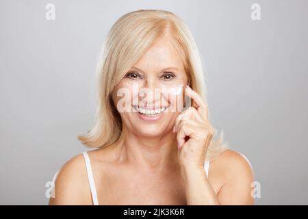 Eine attraktive blonde ältere Frau, die Anti-Age-Creme einlegt. Beauty-Fotografie Stockfoto