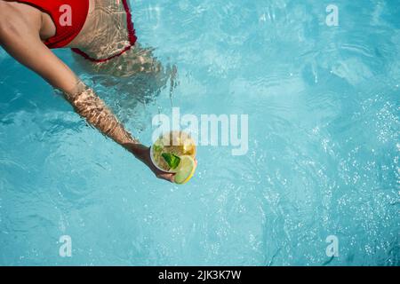 Frau im roten Bikini, die im Sommer einen Mojito-Cocktail im Schwimmbad nimmt. Urlaub und Freiheit Konzept Stockfoto