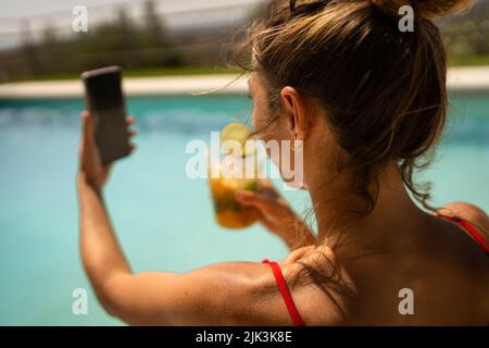 Nahaufnahme einer Frau im roten Bikini, die im Sommer ein Selfie beim Mojito-Cocktail im Pool gemacht hat Stockfoto