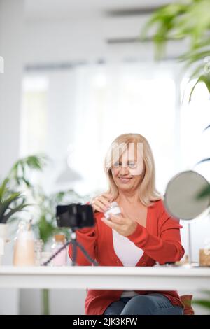 Ein älterer Vlogger, der zu Hause sitzt und über neue Anti-Age-Creme spricht. Stockfoto