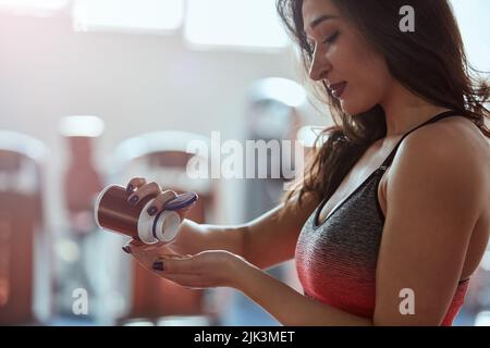 Eine Sportlerin, die im Fitnessstudio steht und vor dem Training Pillen nimmt. Stockfoto