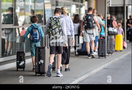 Stuttgart, Deutschland. 30.. Juli 2022. Passagiere gehen mit ihrem Gepäck in ein Flughafenterminal. Das erste Urlaubswochenende in Baden-Württemberg war an den Flughäfen, auf den Straßen, an Bahn- und Fernbusstationen stark ausgelastet. Quelle: Christoph Schmidt/dpa/Alamy Live News Stockfoto