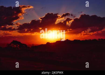 Dramatische Sonnenuntergangsszene über Hügeln auf dem Land mit tiefen Orange-, Rot- und Blautönen Stockfoto