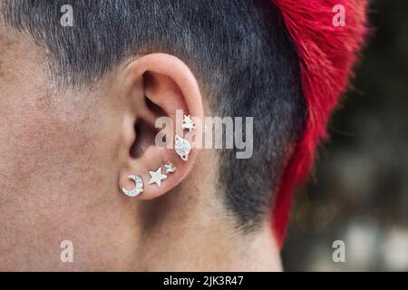 Nahaufnahme eines weiblichen Punkohrs mit silbernen Piercings und einem leuchtend rot gefärbten Mohawk persönlichen Haarstil Stockfoto