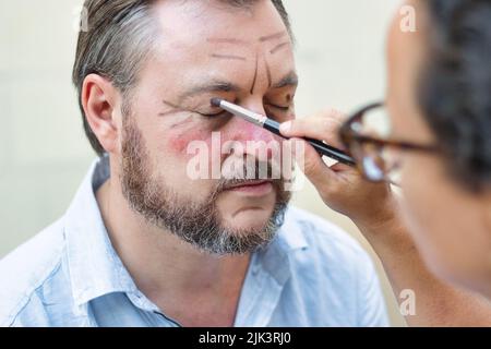 Ein Theaterschauspieler und ein Make-up-Künstler tragen Rouge auf sein Gesicht und seine Linien auf, um ihn älter aussehen zu lassen Stockfoto