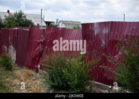 Zaun in der Nähe des Hauses mit Einschusslöchern und Scharapneln nach Schüssen und Kämpfen während der Invasion russischer Truppen in die Ukraine Stockfoto