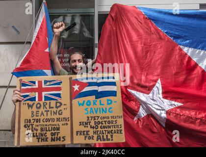 London, Großbritannien. 30.. Juli 2022. Ein Aktivist grüßt mit erhobener Faust mit Plakaten und Fahnen bei einem Protest, der die HSBC in der Oxford Street schloss, Teil einer internationalen Kampagne, die diese und andere Banken auffordert, die Einhaltung der US-Sanktionen gegen Kuba zu beenden, die illegal Finanztransaktionen aus dem Vereinigten Königreich und anderen Bankkonten blockieren und die humanitäre Hilfe für Kuba zur Bewältigung der Covid-Krise eingestellt haben. Trump verhängte weitere 240 Maßnahmen gegen Kuba und Biden hat weitere hinzugefügt, was die Lebensmittel- und Arzneimittelproduktion und die Gesundheitsvorsorge betrifft. Die Kampagne #1c4Cuba fordert Bankkunden dazu auf, 1 zu überweisen Stockfoto