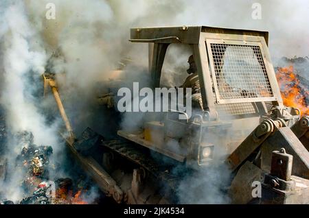 (LOGISTIKBEREICH ANACONDA, Balad, Irak) - Rauch kommt von allen Seiten als Sgt. Richard Ganske, Bataillon des Kampfingenieurs von 84., schiebt den Bulldozer tief in die Flammen der Brandgrube, um brennbare Gegenstände ständig in Flammen zu halten und sie zu entsorgen, damit sie den Posten nicht aufwirren. Bulldozer und Bagger sind die schweren Geräte, die von den 84. EN Mrd. verwendet werden, um Müll in der Brandgrube zu verwalten. Stockfoto