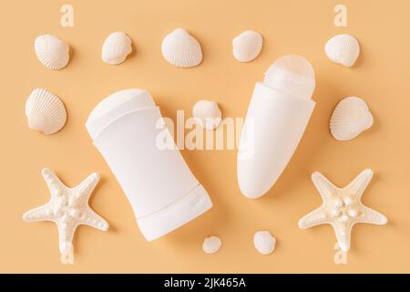 Rollen Sie auf Antitranspirant, festem Deodorant, Seesternen und Muscheln auf pastellorangefarbenem Hintergrund. Konzept von Meeresmineralien-Toilettenartikeln und Naturkosmetik. Stockfoto