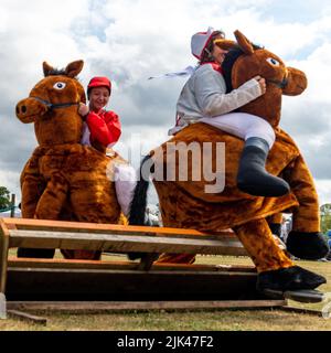 Damerham in der Nähe von Fordingbridge, Hampshire, Großbritannien, 30.. Juli 2022. Pferde und Jockeys springen einen Zaun in der Damerham Fair und Horticultural Show Damerham Derby Fancy Dress Pferderennen. Paul Biggins/Alamy Live News Stockfoto