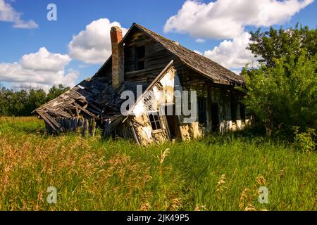 Altes und verwittertes verlassenes Bauernhaus vor einem blauen Himmel mit flauschigen Wolken Stockfoto