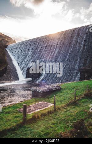 Wasser fließt über den Caban Coch Damm im Elan Valley in Mittelwales, die Sonne geht dahinter unter Stockfoto