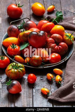 Tomaten verschiedener Sorten und Größen auf einem eisernen Tablett auf einem Holztisch. Stockfoto