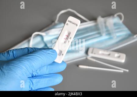 Nahaufnahme eines medizinischen Mitarbeiters, der blaue Operationshandschuhe trägt und ein covid-19-Testgerät hält, das ein positives Ergebnis in seiner Hand mit Schutzwirkung zeigt Stockfoto