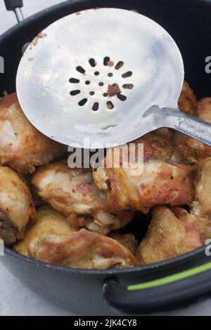 Die Hähnchenschenkel werden in einem gusseisernen Kessel gebraten. Kochen im Freien. Nahaufnahme. Stockfoto