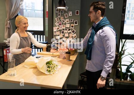Ein Mann zahlt für Blumen in einem Blumengeschäft mit einer Kreditkarte über ein drahtloses Bankterminal Stockfoto