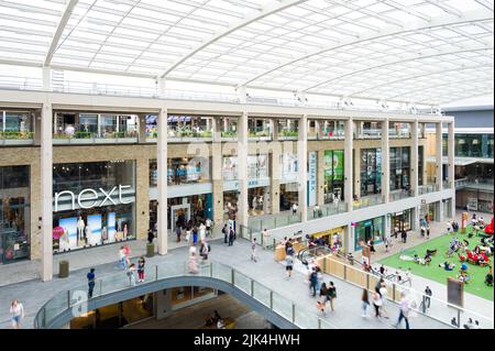 Das Innere des Westgate Shopping Centre mit Menschen, die an Einzelhandelsgeschäften vorbeilaufen, Oxford, Großbritannien Stockfoto