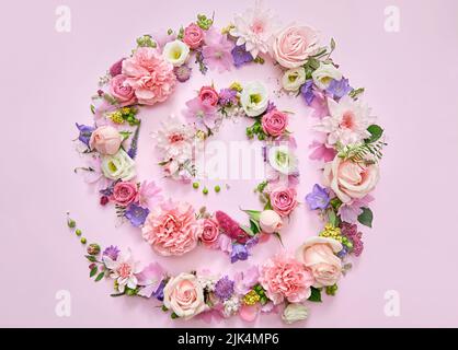 Blumen und Blätter spiralförmig auf rosa floralem pastellfarbenem Hintergrund. Flach liegend, Draufsicht Stockfoto