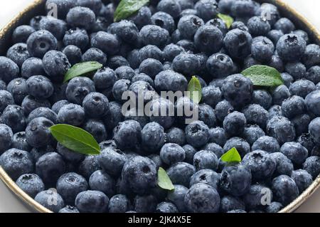 Heidelbeeren mit grünen Blättern in Wassertropfen verschließend. Frische saftige blaue Beeren. Stockfoto