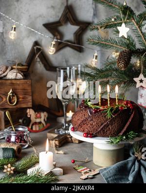 Stillleben mit Weihnachtsgebundener Kuchen mit Kerzen. Traditionelles festliches Dessert auf weihnachtlichen Hintergrund. Vertikale Ausrichtung Stockfoto