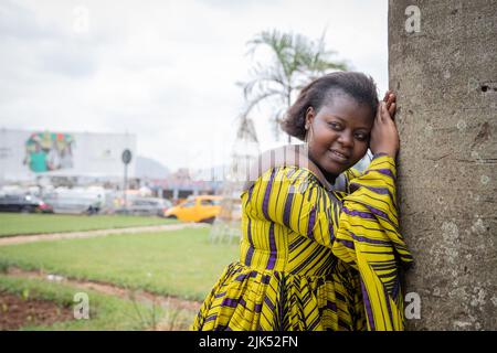 Junge ernsthafte afrikanische Frau, die sich an einem Baum lehnt, wird fotografiert. Stockfoto