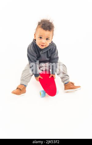 Fünf Jahre altes afroamerikanisches Kleinkind, das auf dem Skateboard sitzt und in die Kamera blickt - weißer Hintergrund. Hochwertige Fotos Stockfoto