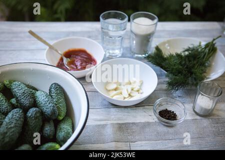 Der Prozess der Konservierung eingelegter Gurken für den Winter. Zutaten für die Konservierung: Dill, geschälter Knoblauch, Paprika, Ketchup, Salz, Zucker, Rebe Stockfoto