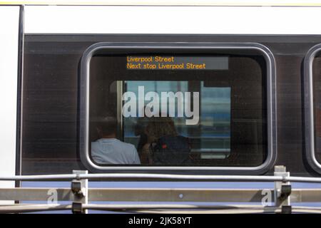 Ein Paar sitzt zusammen in einem Zug. Außenansicht des Zuges mit einem Schild mit der Aufschrift „Liverpool Street“ am Fenster eines Londoner Bahnhofs Stockfoto