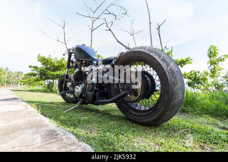 Ein Custom Chopper Motorrad geparkt auf Gras neben einem tropischen Strand. Rattenrad, niedriger Fahrer, Honda-Motor Stockfoto