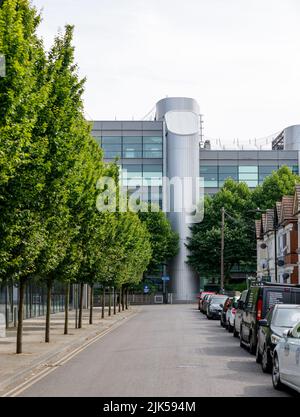 Campus der University of Essex Southend von der Elmer Avenue aus gesehen. Modernistisches Gebäude, von Bäumen gesäumte Straße, geparkte Autos. Stockfoto