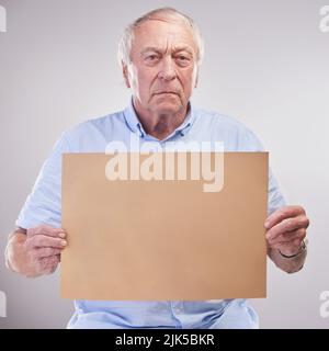 Das ist so ernst wie es geht. Studioaufnahme eines älteren Mannes mit einem leeren Schild vor grauem Hintergrund. Stockfoto