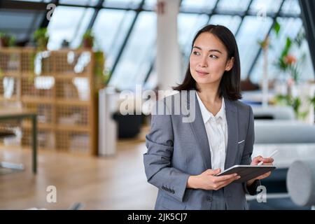Junge asiatische Geschäftsfrau, die im Büro mit einem digitalen Tablet steht. Stockfoto
