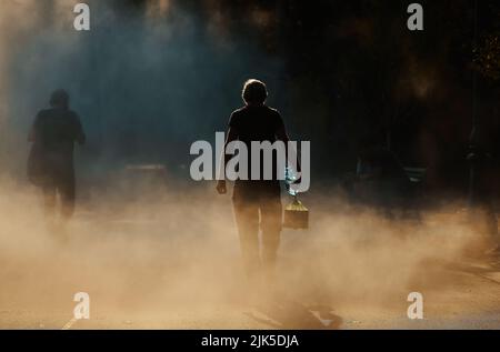 Bucharest, Romania - July 26, 2022: A man carrying a water bottle walks through the fine spray of a fountain on a very hot day This image is for edito Stockfoto