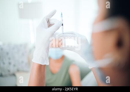 Keine Luftblasen für meine süße nanna. Nahaufnahme einer nicht erkennbaren Ärztin, die die Spritze überprüft, bevor sie ihre Patientin injiziert. Stockfoto