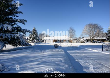 Schneebedeckte Auffahrt führt hinaus und zum schneebedeckten Bungalow auf der anderen Straßenseite. Stockfoto