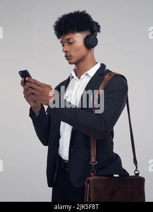Ein Podcast, mit dem sich jeder Profi identifizieren kann. Studioaufnahme eines jungen Geschäftsmannes mit Smartphone und Kopfhörer vor grauem Hintergrund. Stockfoto