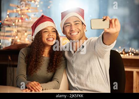 Zwei junge Geschäftsleute, die ein Selfie machen, während sie Weihnachten bei der Arbeit feiern. Stockfoto