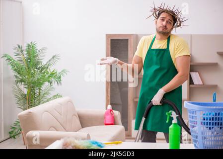 Junger männlicher Auftragnehmer, der auf dem Kopf einen stacheligen Kranz trägt und Hausarbeit leistet Stockfoto
